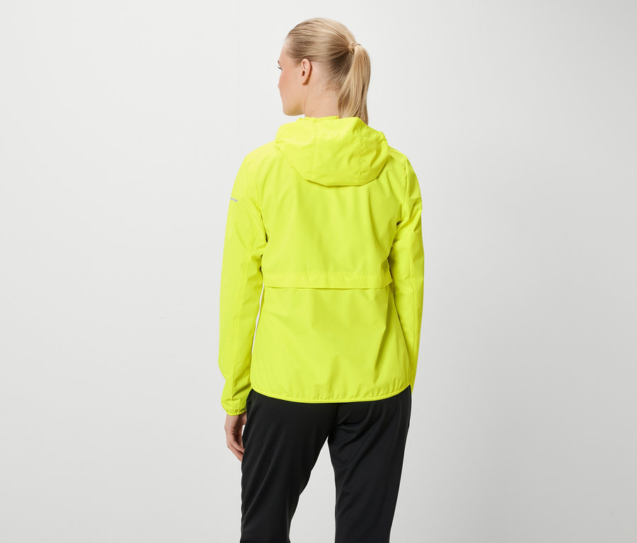 Vue de dos, une femme aux cheveux blonds attachés en queue de cheval porte une veste à capuche jaune fluo et un pantalon noir.
