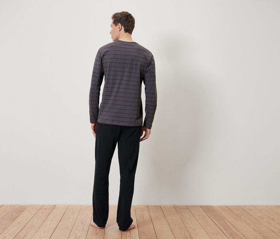 Un homme, vu de dos, porte un T-shirt de nuit à rayures grises à manches longues et un pantalon de nuit noir.