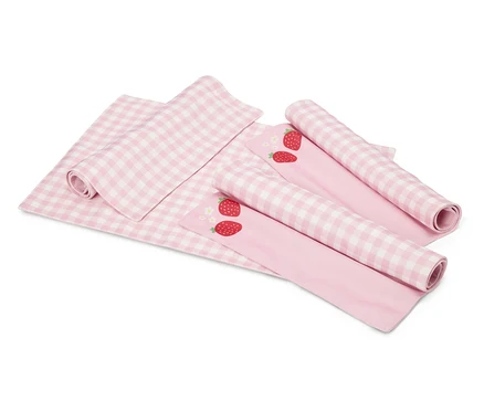 Sur un fond blanc se trouvent une couverture à carreaux rose et blanc et deux tissus roses avec des motifs de fraises, partiellement enroulés.