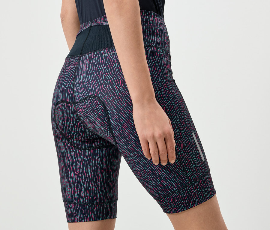 Gros plan d'une femme portant un short de cyclisme à motifs avec une taille noire et une languette réfléchissante sur la jambe.