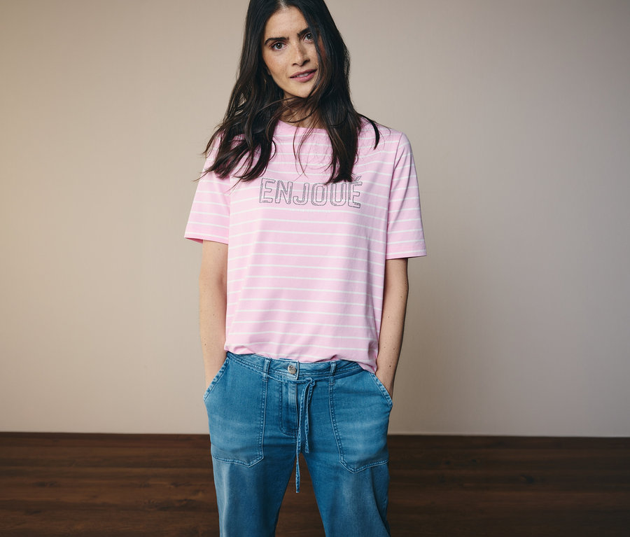 Femme portant un jean et un T-shirt CECIL rose et blanc rayé avec le mot ENJOUE.