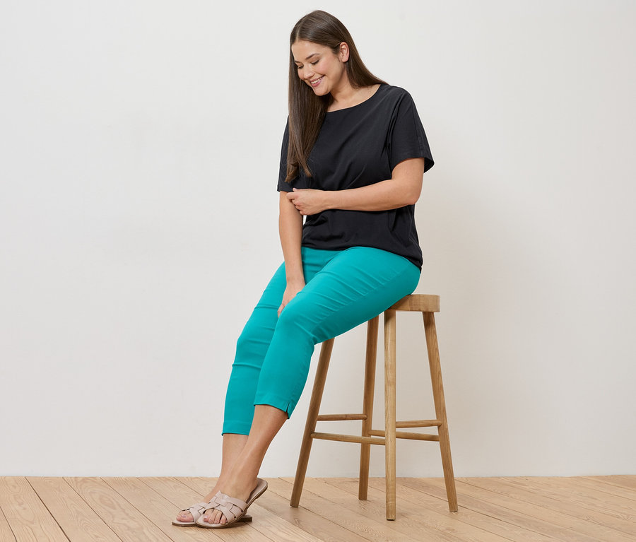 Femme assise sur un tabouret, portant un blusenshirt noir et un pantalon stretch 7/8 bleu azur.