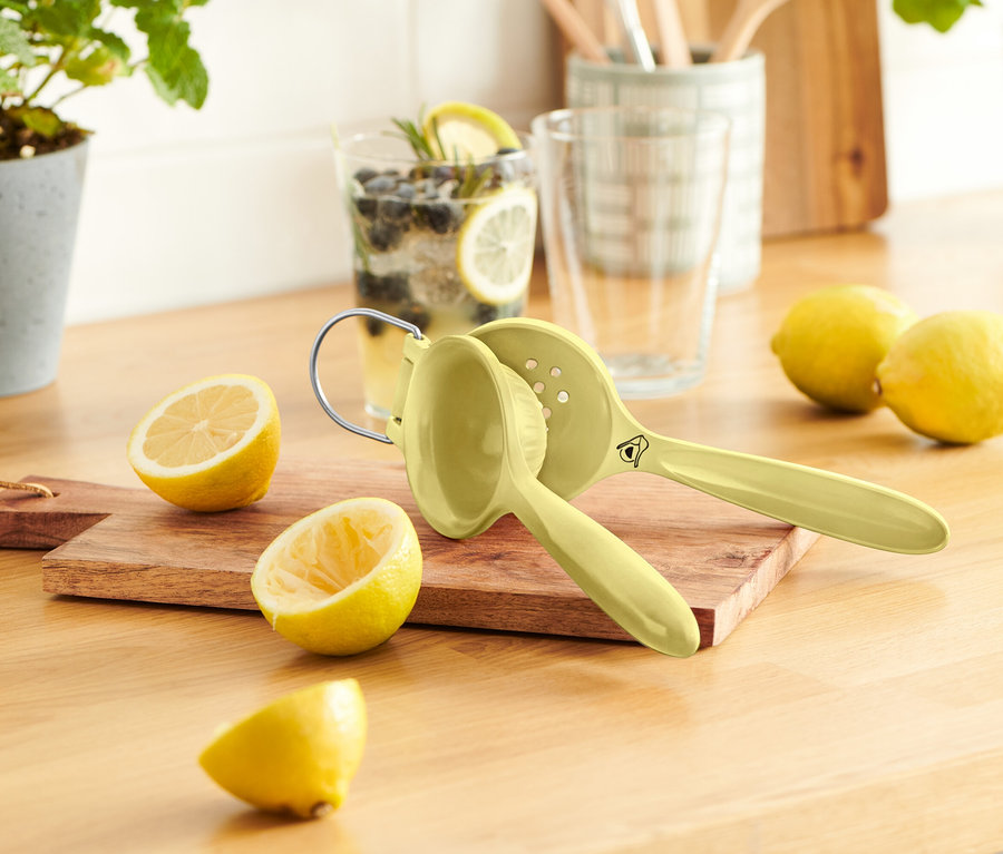 Sur une table en bois se trouvent quelques citrons, un presse-agrumes et un verre de limonade.