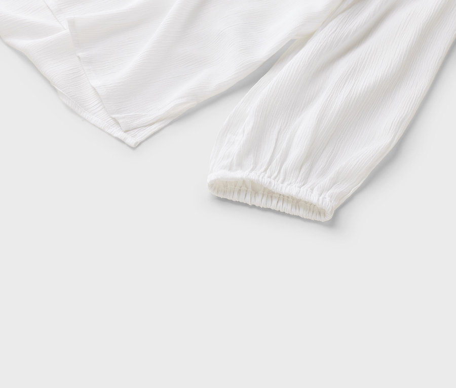 Gros plan d'un chemisier blanc à manches longues et poignets froncés sur un fond blanc.