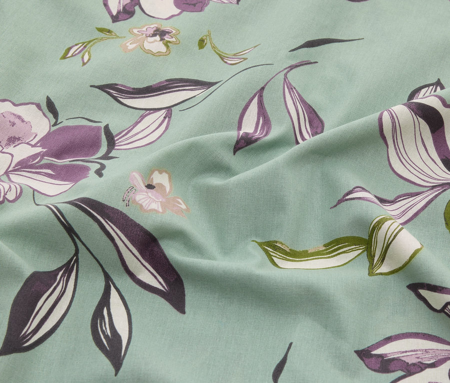 Gros plan d'un tissu vert menthe avec un motif floral dans les tons de violet, de blanc et de vert.