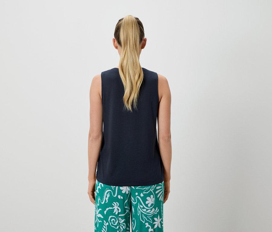 Vue arrière d'une femme avec une queue de cheval blonde portant un débardeur bleu marine et un pantalon vert à motifs.