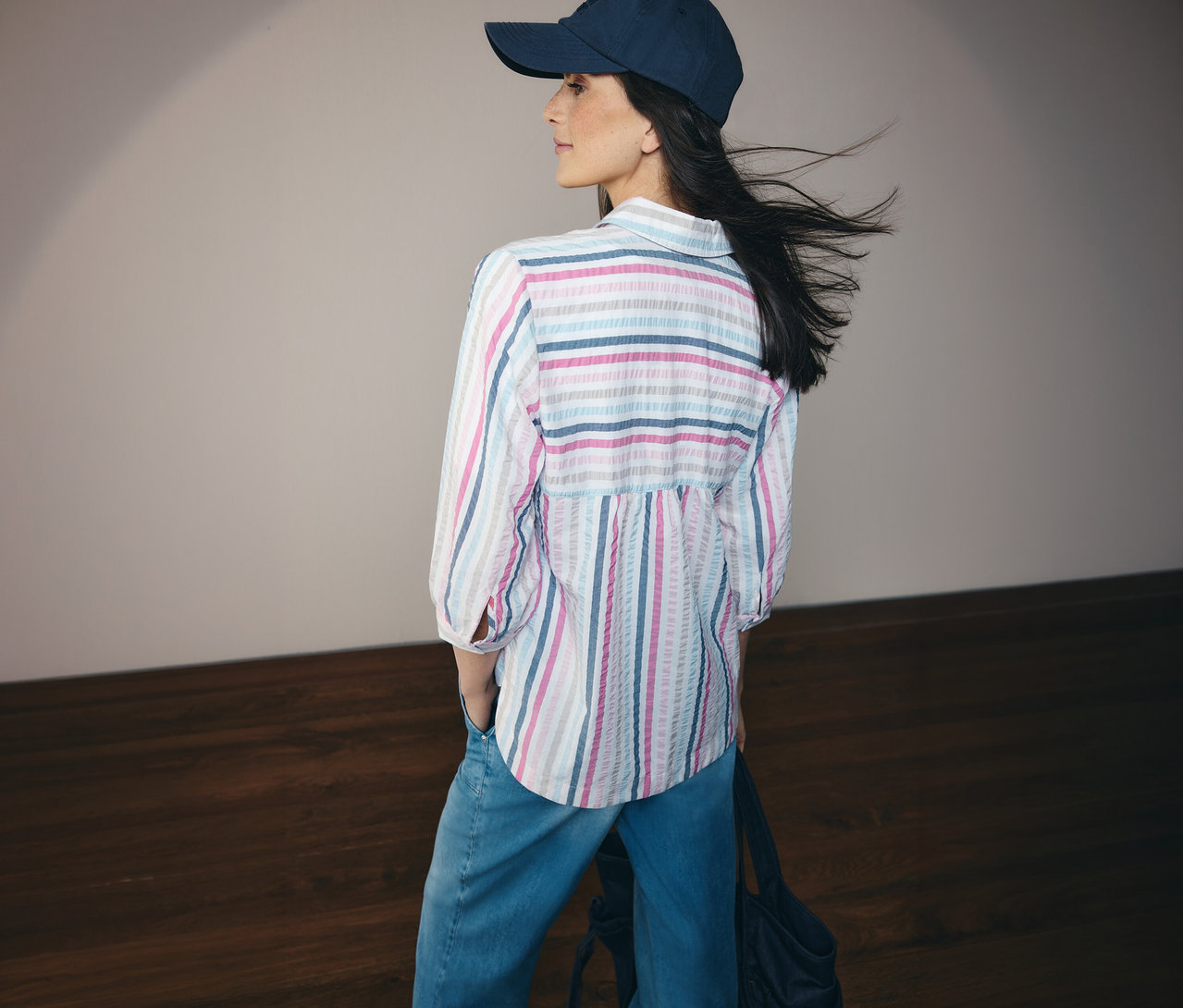 Femme portant un jean, un chemisier CECIL rayé bleu et une casquette, vue de dos.