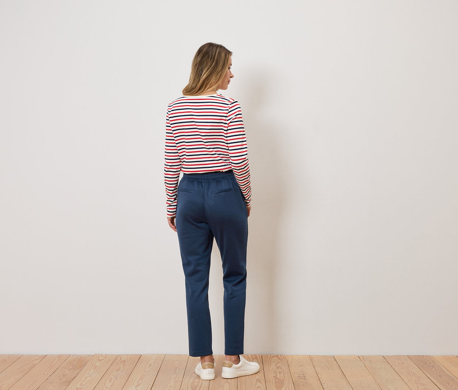 Femme vue de dos portant un t-shirt rayé à manches longues, un pantalon bleu et des baskets blanches.