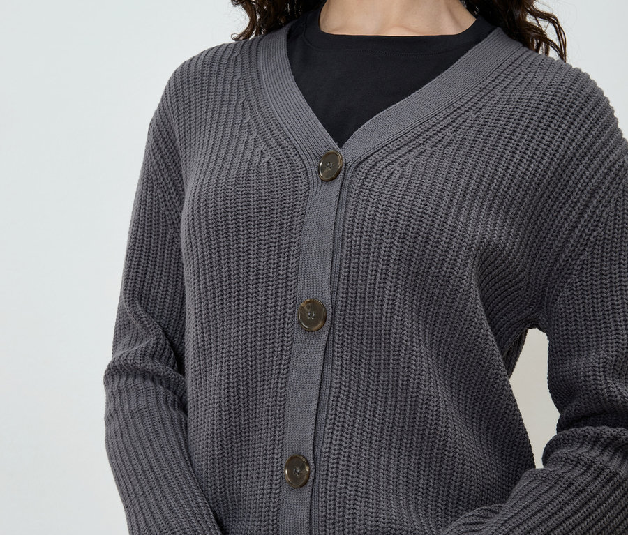 Une femme porte un cardigan gris sur un t-shirt noir.