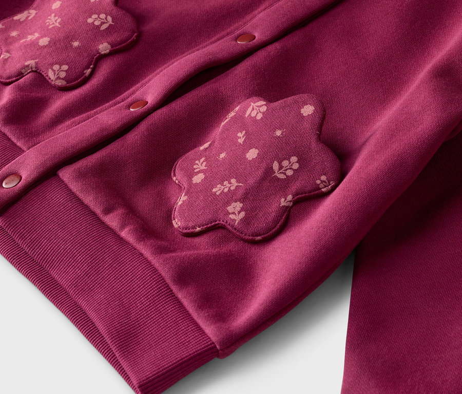Gros plan sur un cardigan bordeaux avec des appliqués de fleurs et des boutons, ainsi qu'un pantalon assorti.