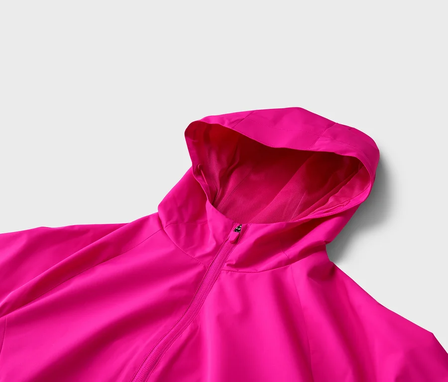 Gros plan d'une veste rose à capuche et fermeture éclair sur un fond neutre.