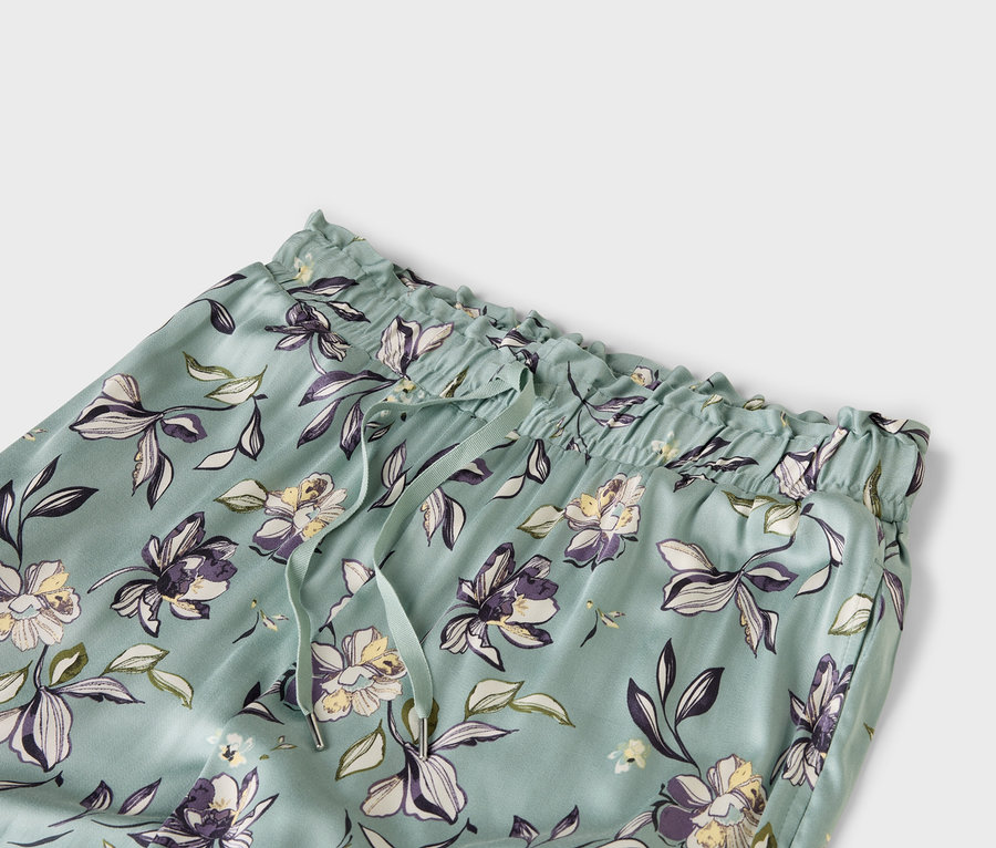 Gros plan d'un pantalon bleu clair avec un motif floral, une taille élastique et un cordon de serrage.