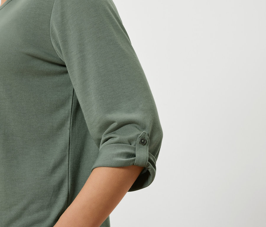 Gros plan d'un haut vert olive à manches trois-quarts attachées par un bouton.
