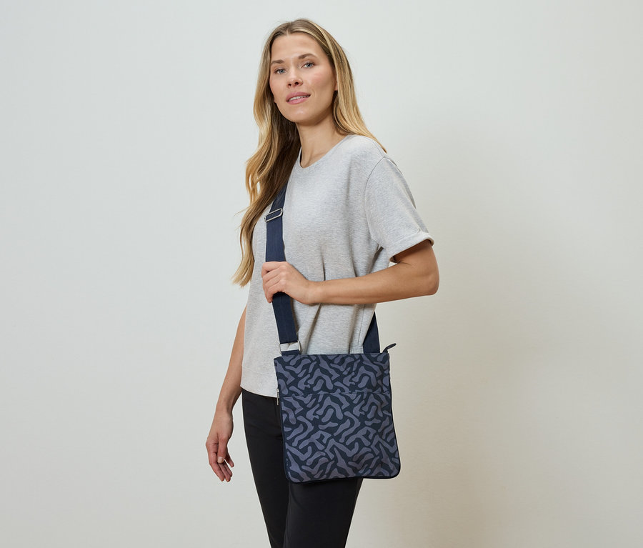 Femme portant un sac à bandoulière bleu marine avec un motif abstrait.