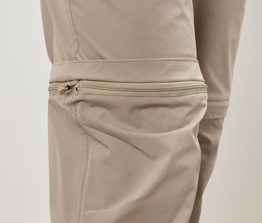 Gros plan d'un pantalon beige avec un détail de fermeture éclair au niveau du genou.