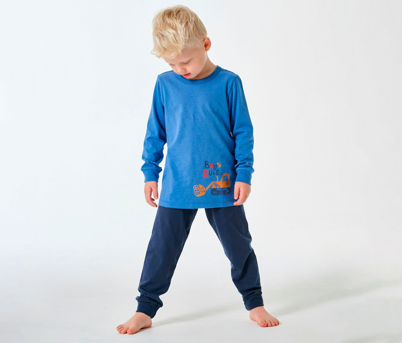 Garçon blond portant un pyjama long pour enfant SCHIESSER avec un motif de tractopelle, pieds nus sur fond blanc.