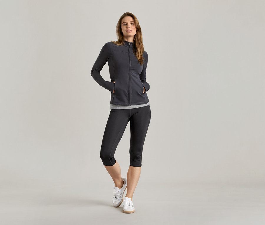 Femme en tenue de sport avec 2 hauts noir/gris sous une veste.
