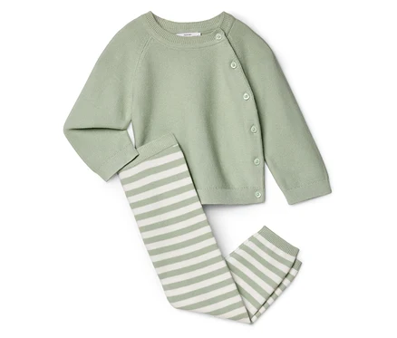 Un cardigan vert clair boutonné est posé à côté d'un legging rayé sur un fond blanc.