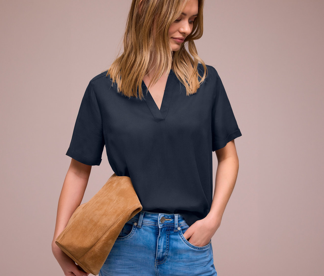 Femme portant un jean et une blouse en maille Street One bleu marine, tenant un sac en daim marron.