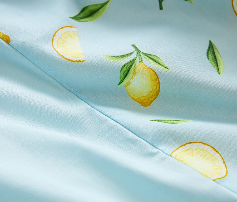Gros plan d'un tissu bleu clair avec un motif de citrons et de feuilles et une couture.