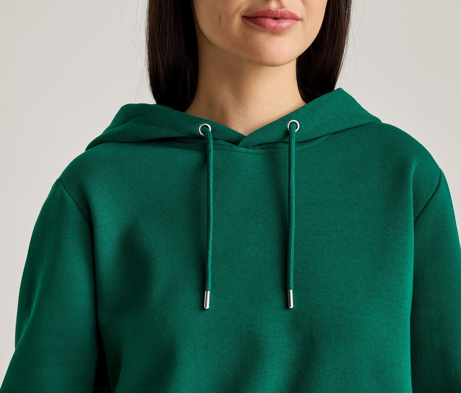 Gros plan d'une femme aux cheveux brun foncé portant un sweat à capuche vert avec cordon de serrage.