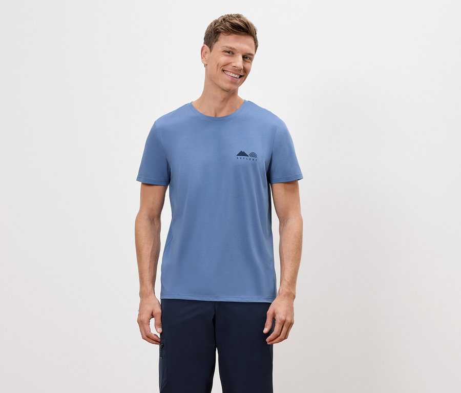 Un homme porte un t-shirt bleu avec un petit motif de montagne et d'arc-en-ciel et un short bleu marine.