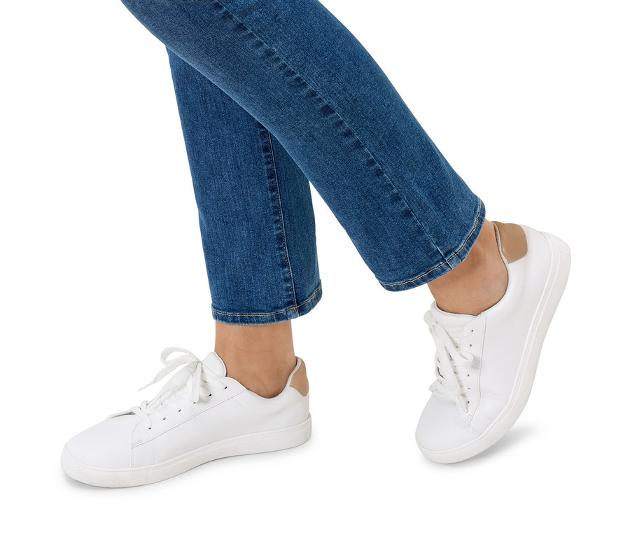Jambes d'une personne portant un jean bleu et des baskets blanches.