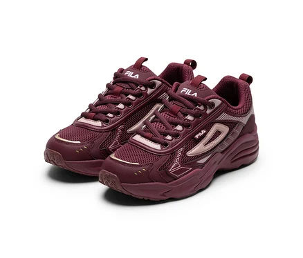Une paire de baskets Fila bordeaux avec des empiècements en mesh et synthétiques, des accents dorés et des logos Fila blancs, sur fond blanc.