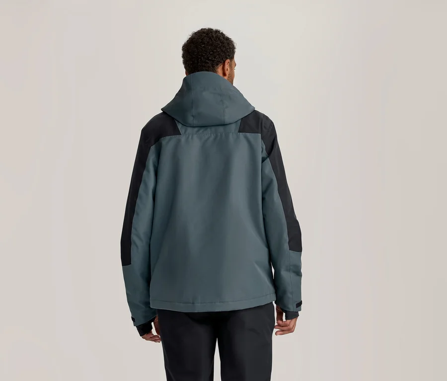 Personne vue de dos, portant une veste à capuche bleu-vert foncé et noire, et un pantalon noir.