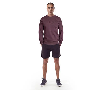 Homme debout portant un sweat-shirt rouge foncé avec un logo Fila, un short noir et des baskets foncées.