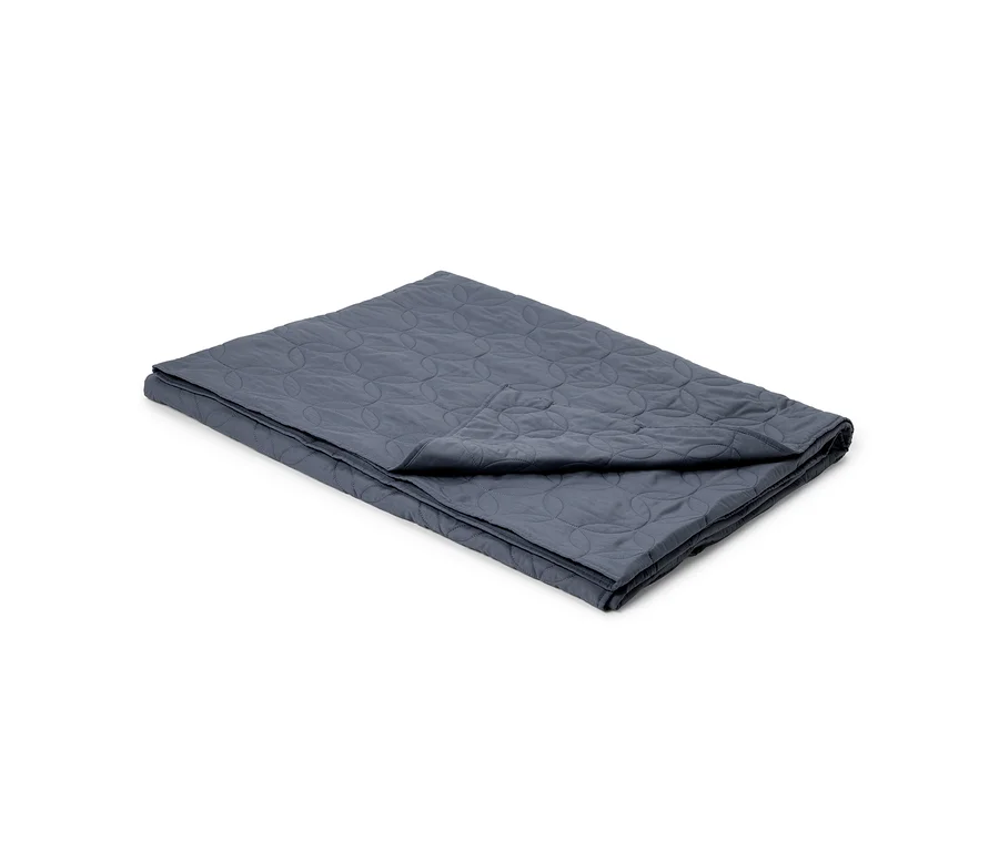 Une couverture matelassée gris foncé, pliée, avec un motif de cercles entrelacés.