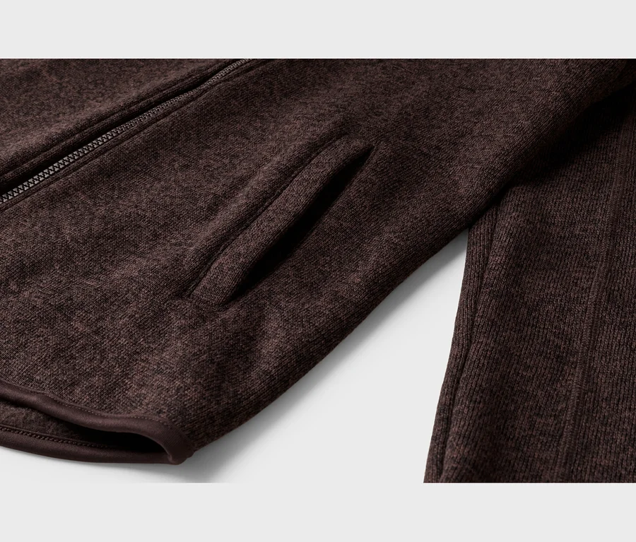 Gros plan d'une veste en maille chinée marron foncé, avec une fermeture éclair partiellement visible, une poche latérale intégrée et une texture côtelée à droite.