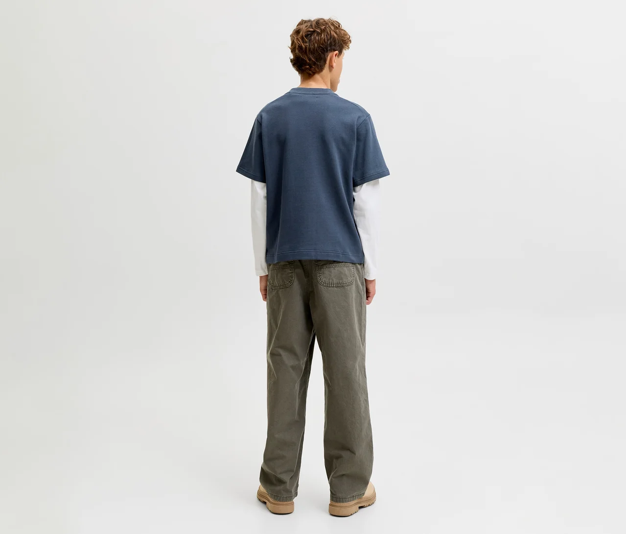 Personne de dos, portant un t-shirt double couche Jack&Jones composé d'un t-shirt bleu à manches courtes sur un t-shirt blanc à manches longues, un pantalon vert olive et des chaussures marron clair.
