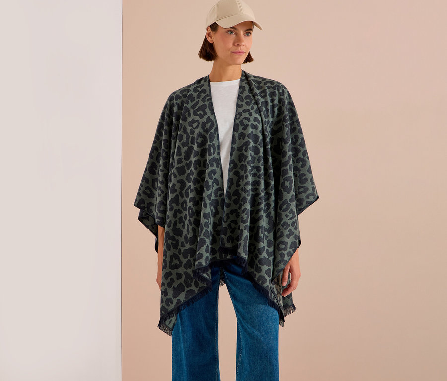 Femme portant un poncho CECIL vert foncé à imprimé léopard avec franges, un t-shirt blanc, un jean bleu et une casquette beige.