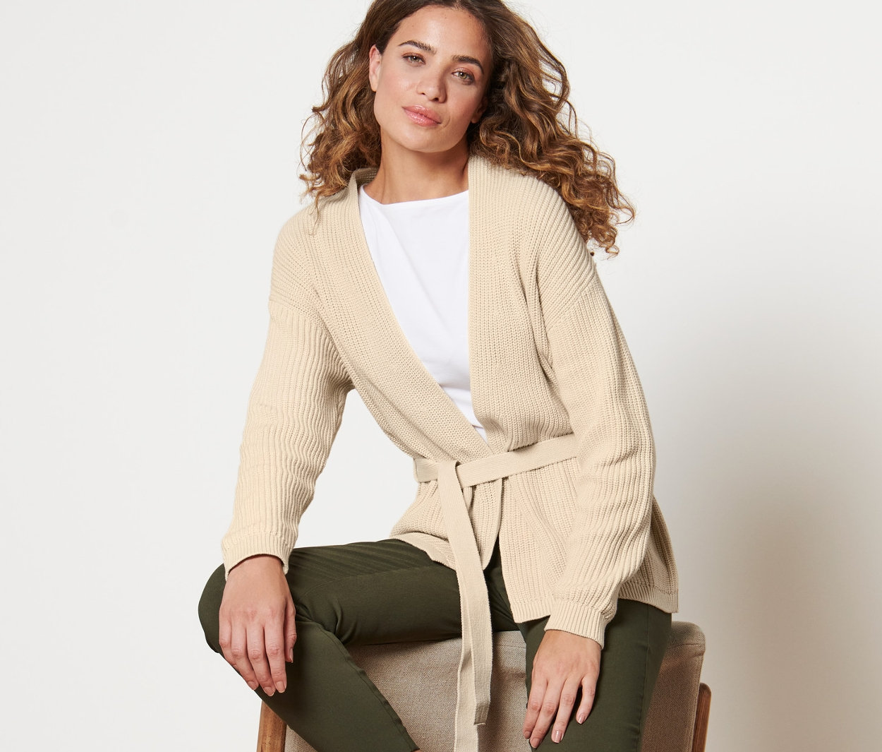 Femme assise sur une chaise portant un cardigan cache-cœur.