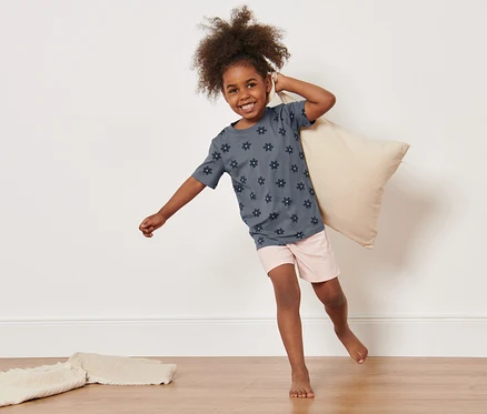 Fillette tenant un oreiller et portant 2 pyjamas pour tout-petits.