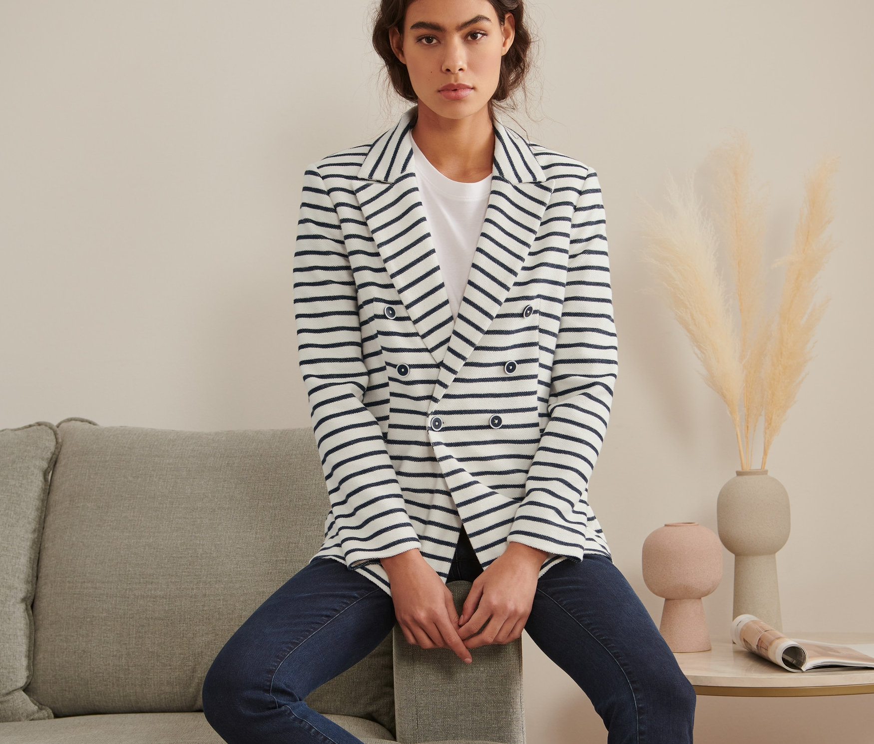 Une femme assise sur un canapé gris portant un blazer molletonné à rayures.
