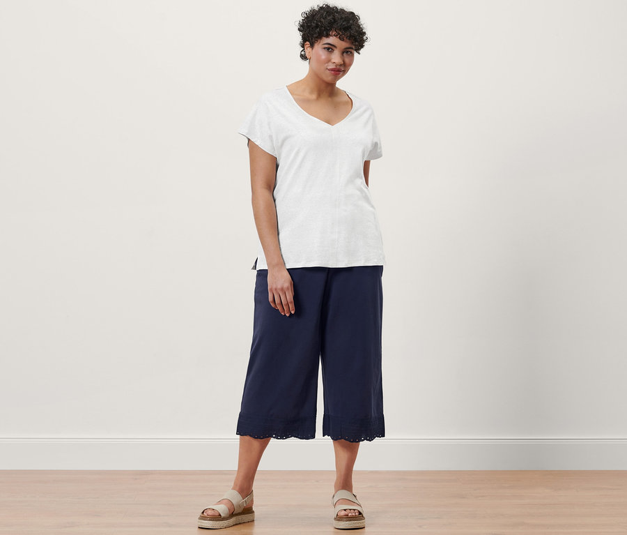 Une femme pose avec un t-shirt en lin mélangé blanc crème, une jupe-culotte bleu marine à broderie et des sandales à plateforme en cuir.