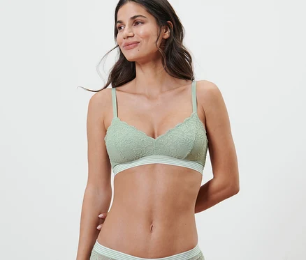Une femme portant un ensemble de lingerie en dentelle vert clair avec un soutien-gorge souple.