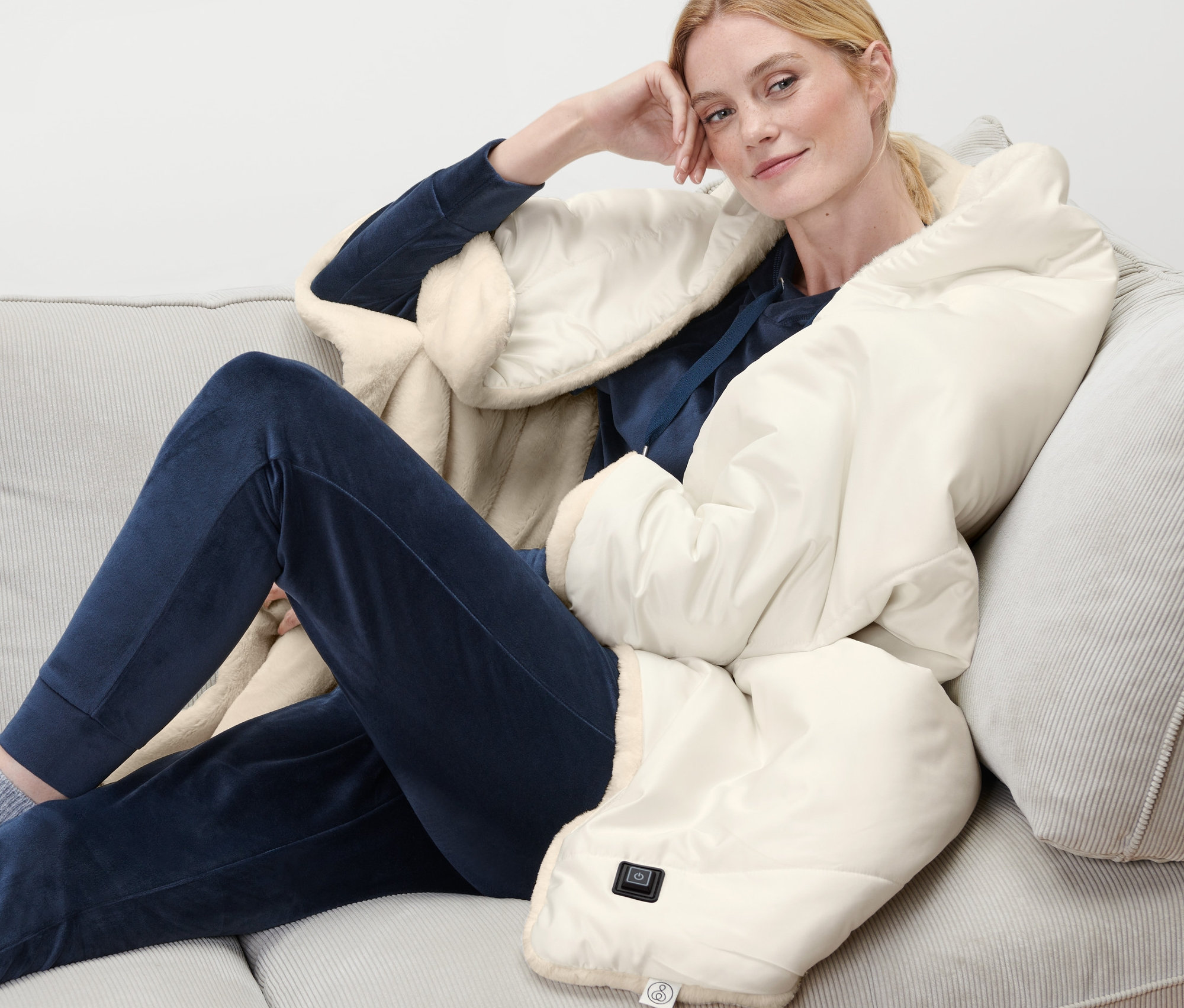 Femme assise sur un canapé avec un poncho chauffant à batterie.