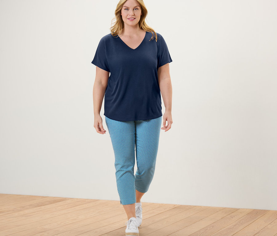Femme marchant et portant un pantalon stretch 7/8 imprimé intégral, un t-shirt à col en V et des baskets.