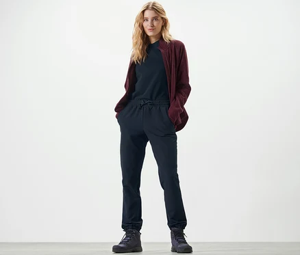 Une femme blonde se tient debout, les mains dans les poches d'un pantalon de jogging en softshell.