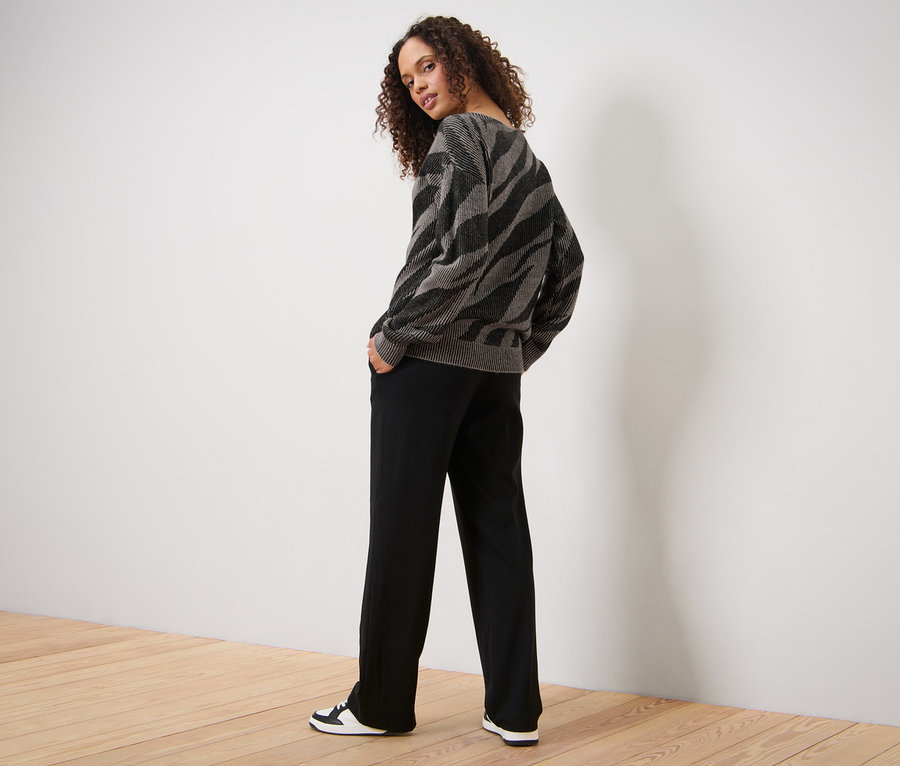 Femme posant en pull en maille jacquard, pantalon noir et baskets.