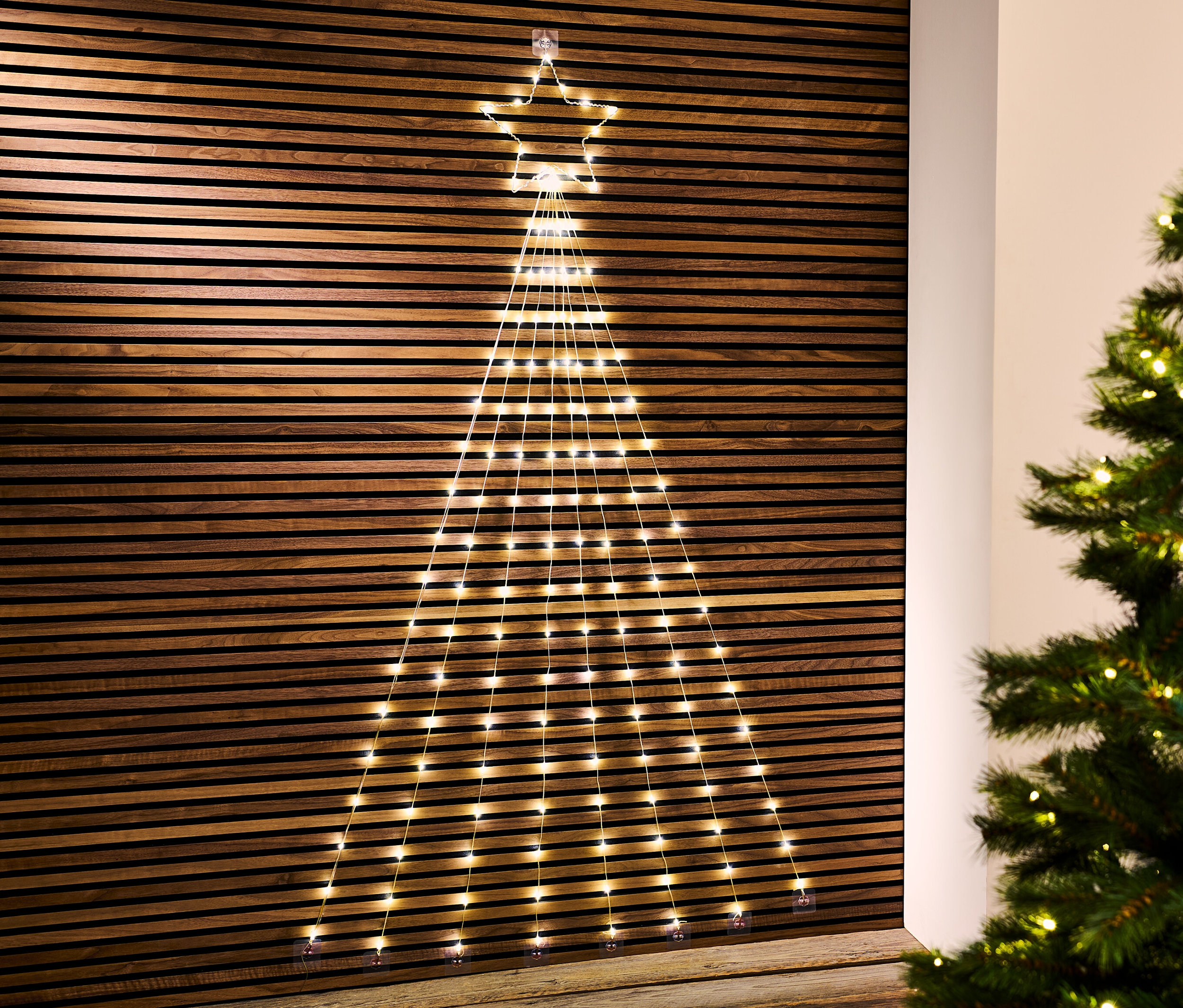 Une silhouette LED en forme de sapin de Noël est accrochée à un mur en bois.