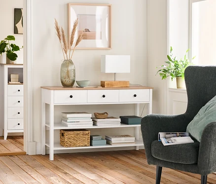 Intérieur d'un salon avec un fauteuil rembourré anthracite, une console à tiroirs et une lampe de table avec pied en bois.