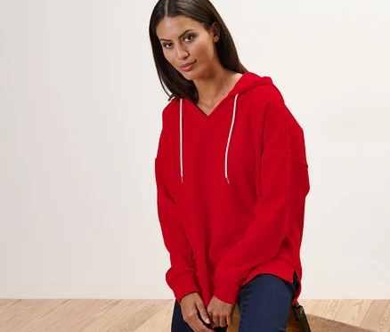 Une femme est assise sur une chaise et porte un sweat à capuche rouge.