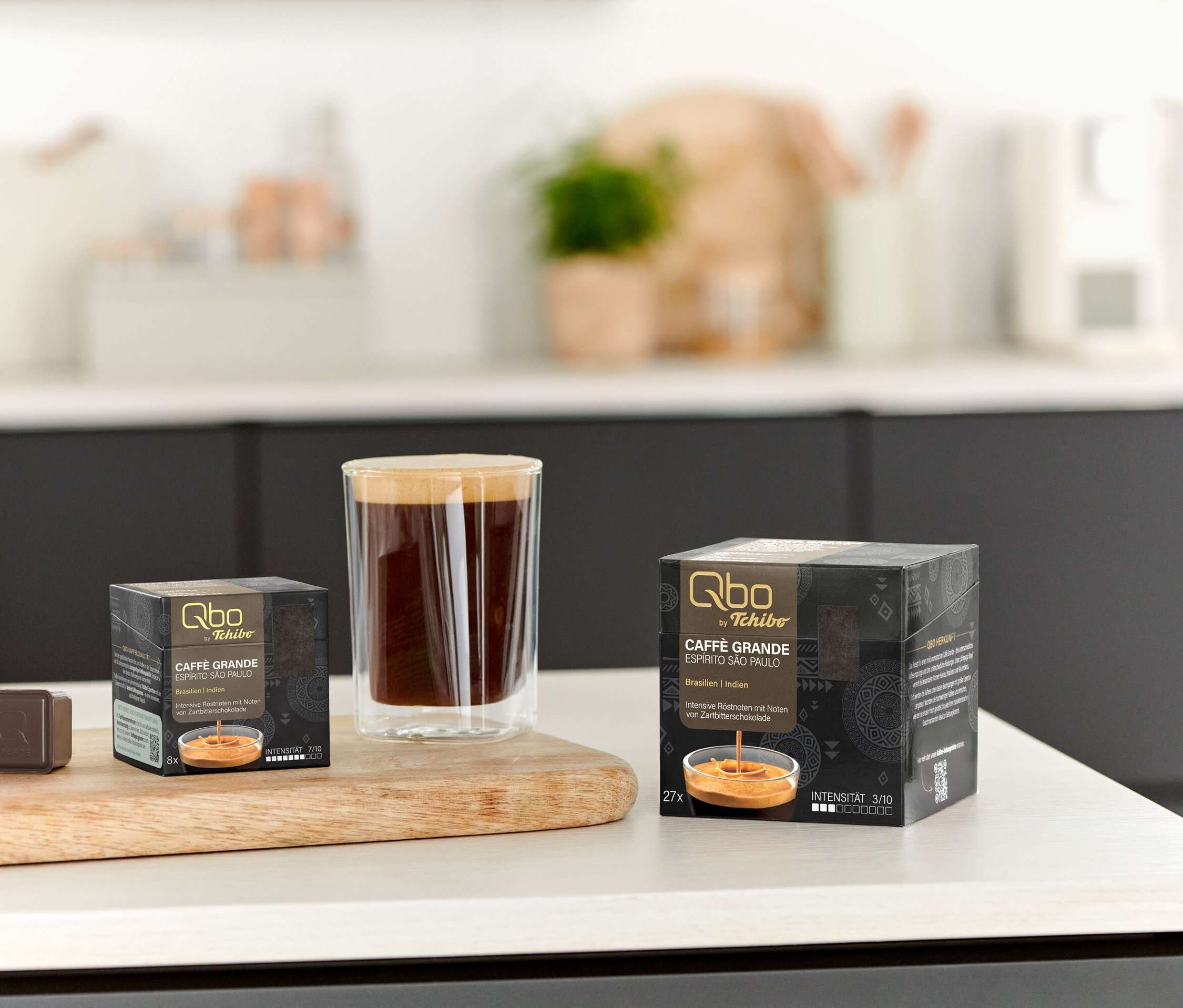 Sur une table, une tasse de café et des paquets de Qbo Caffè Grande ESPÍRITO SÃO PAULO de 8 et 27 capsules.