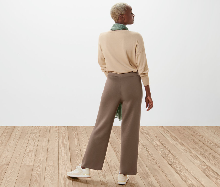 Une femme vue de dos porte un pull beige et un pantalon en maille marron.