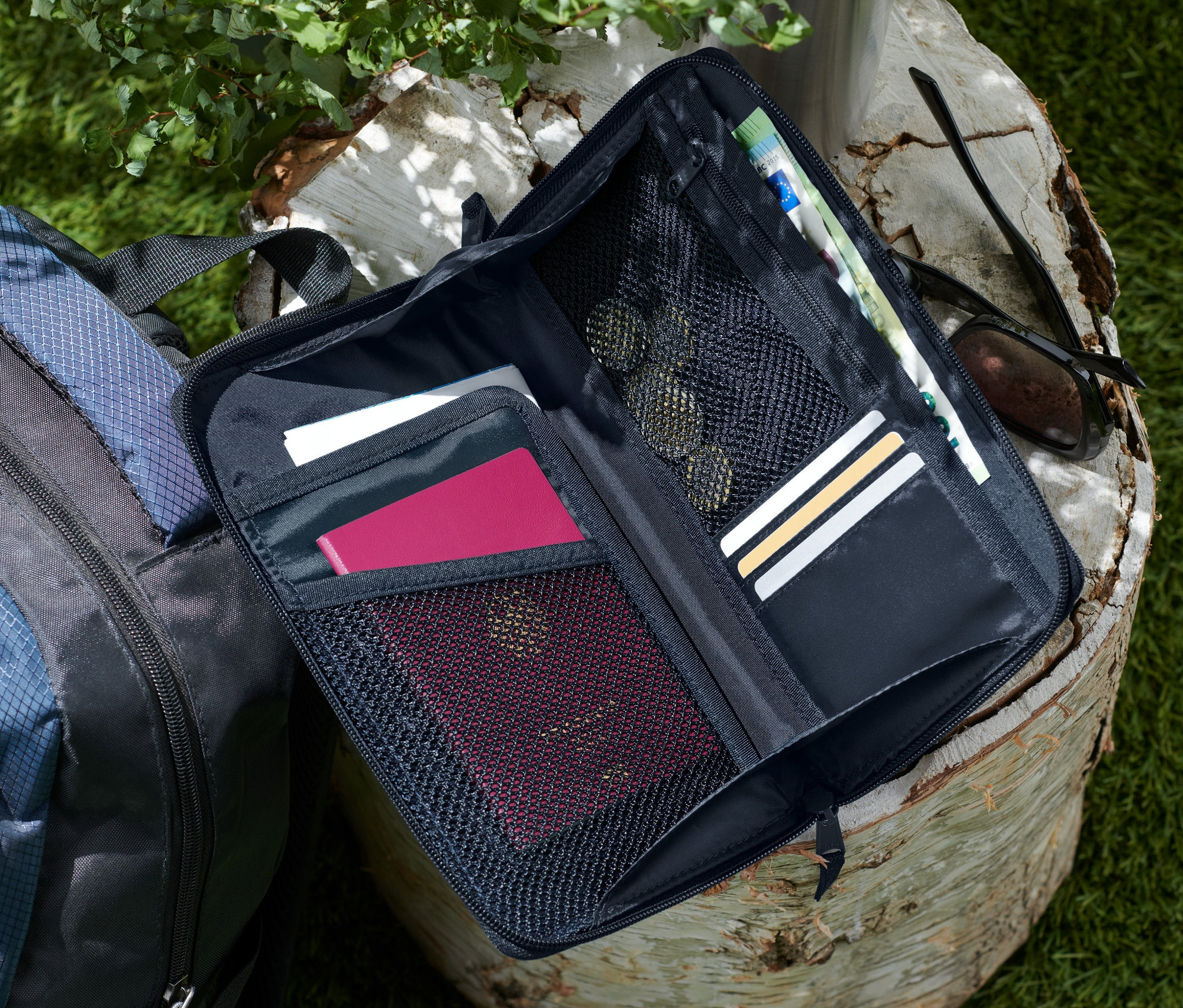 Un porte-documents noir ouvert est posé sur une souche d'arbre à côté d'un sac à dos bleu et noir.