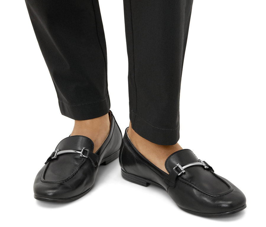 Pieds portant des mocassins en cuir noirs.